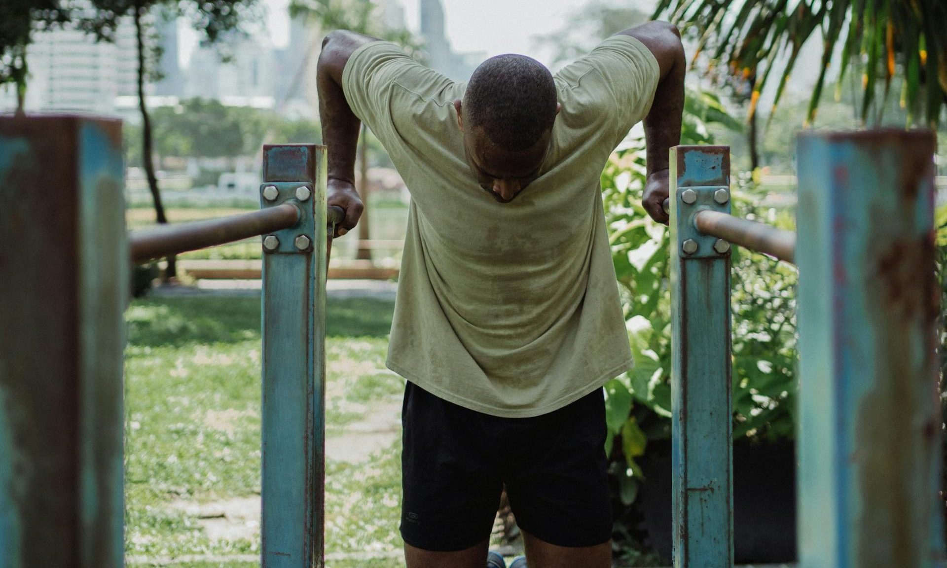 Man wearing a T-shirt and shorts doing dips exercise on metal bars outside