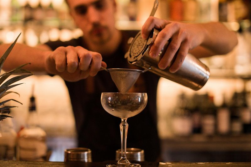 Bartender pouring drink through strainer