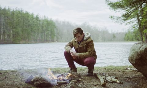 A man sitting next to a campfire near a lake