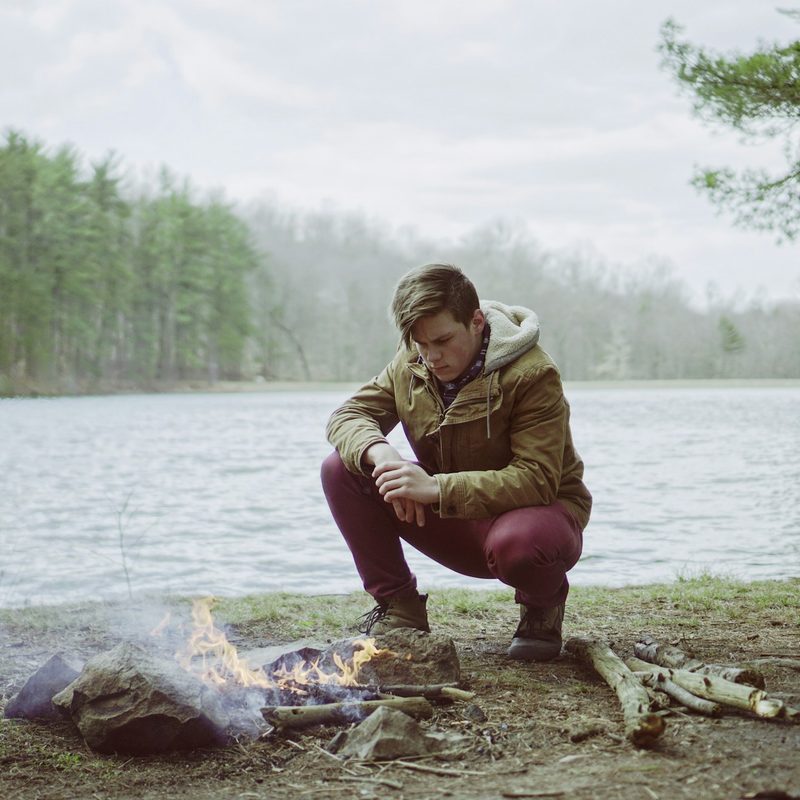A man sitting next to a campfire near a lake