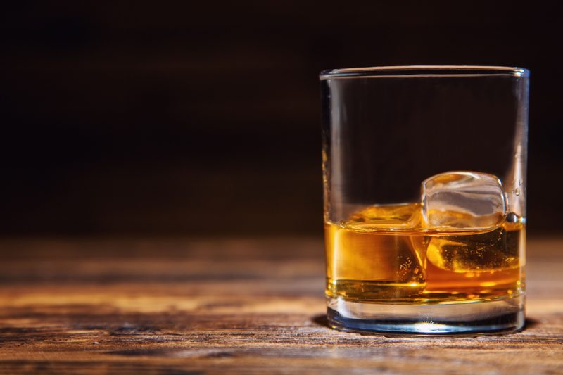 Glass of whiskey with ice cubes served on wooden planks