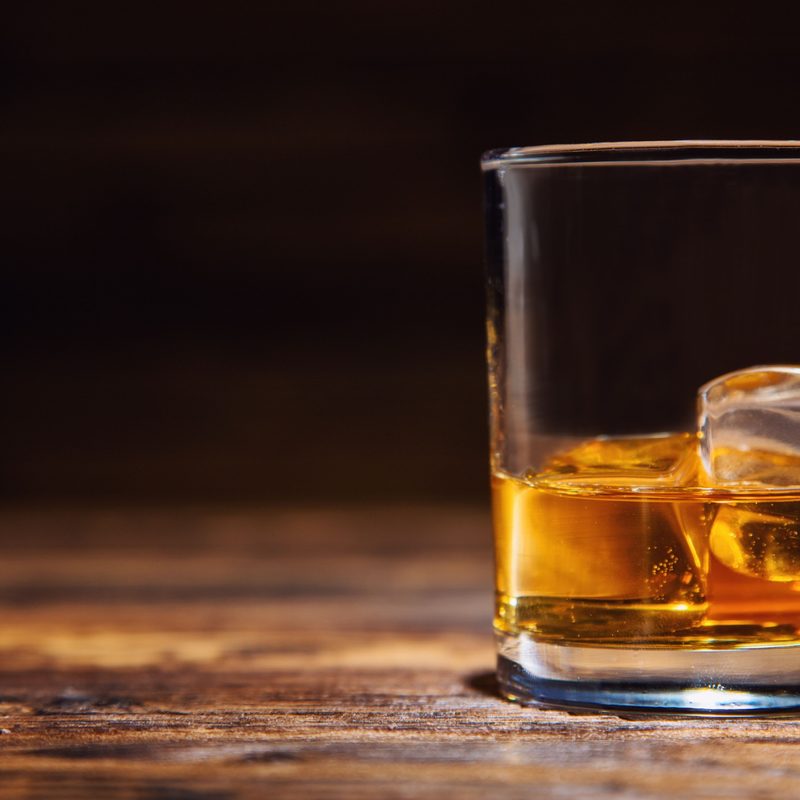 Glass of whiskey with ice cubes served on wooden planks