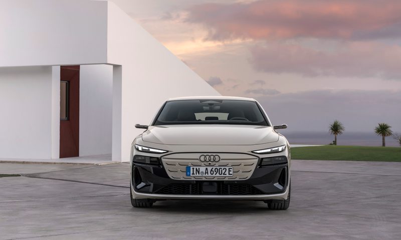 2025 Audi e-tron Sportback parked beside a house with a lawn and ocean in the background.