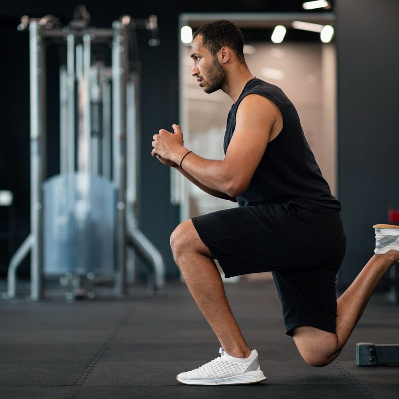 Man in gym with shorts doing Bulgarian split squat exercise in gym