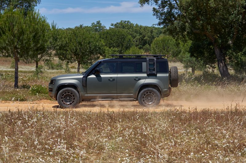 Land Rover Defender OCTA driving on a dirt road in field and forest.