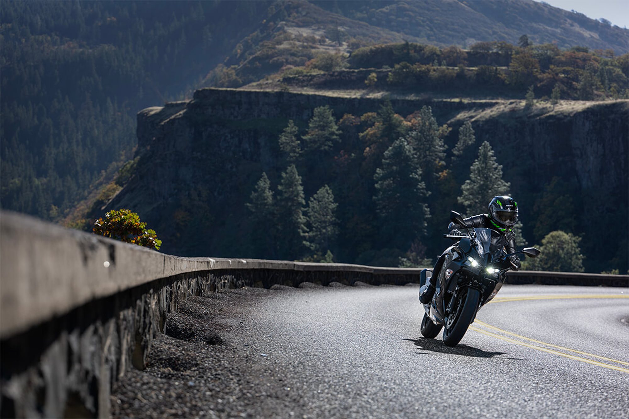Rider on a black 2024 Kawasaki 500 on a curve on a road through mountains.