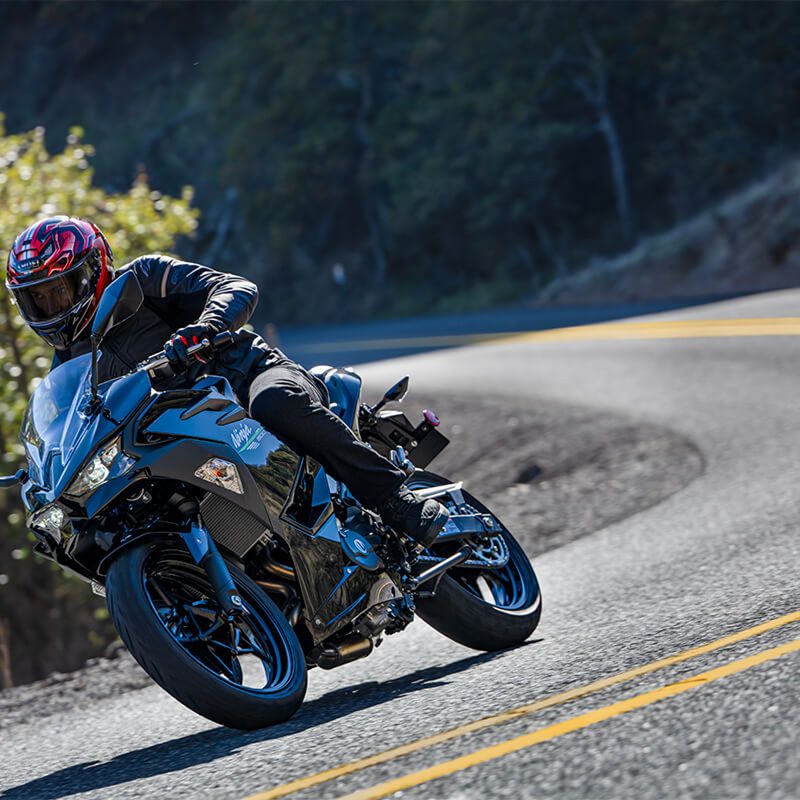 Rider on a blue 2024 Kawasaki 500 on a curve on a road through mountains