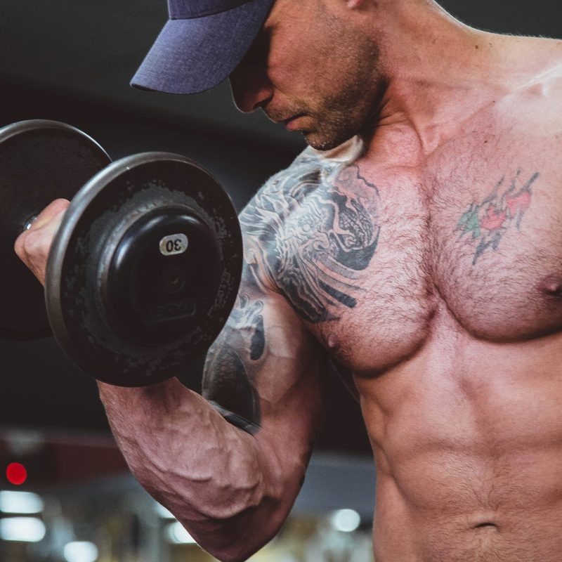 Man wearing hat shirtless lifting weights in gym exercise zottman curl