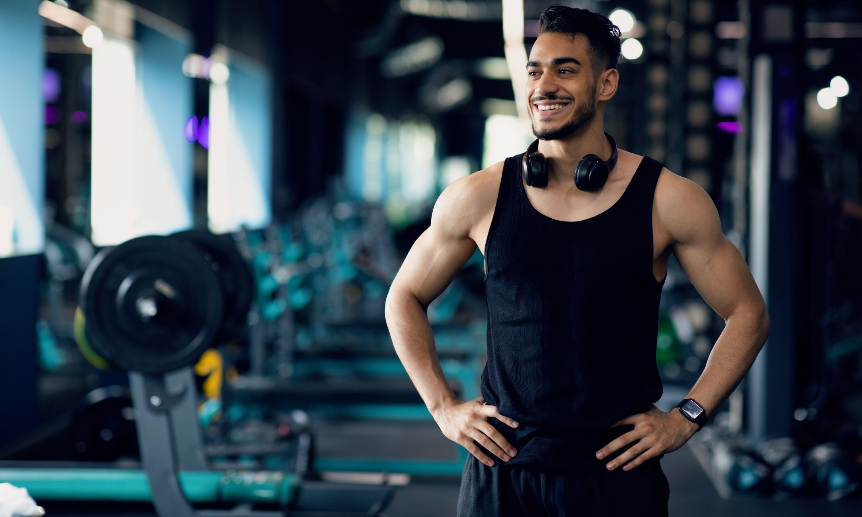 Man in gym wearing a black tank top standing smiling black headphones