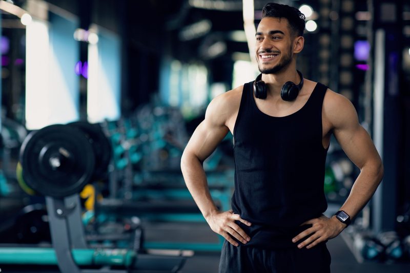 Man in gym wearing a black tank top standing smiling black headphones