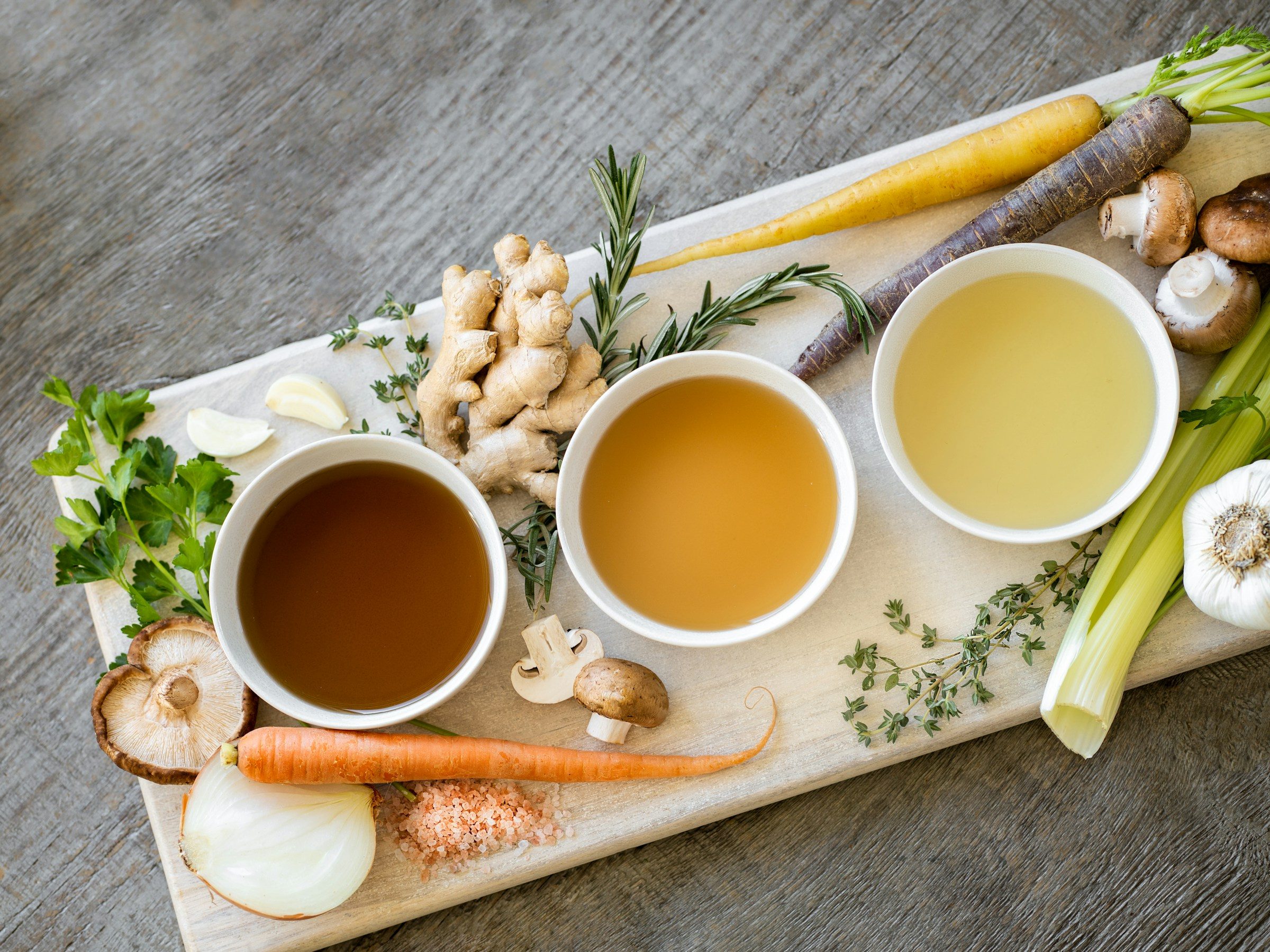 Trio of broths on wooden board with vegetables