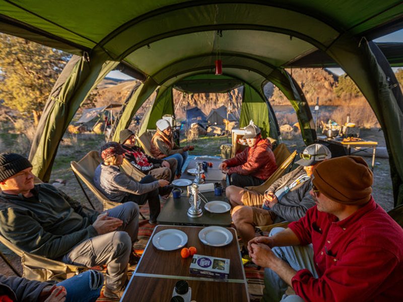 Large group sitting around a long table inside a DoD Kamaboko Super Tent
