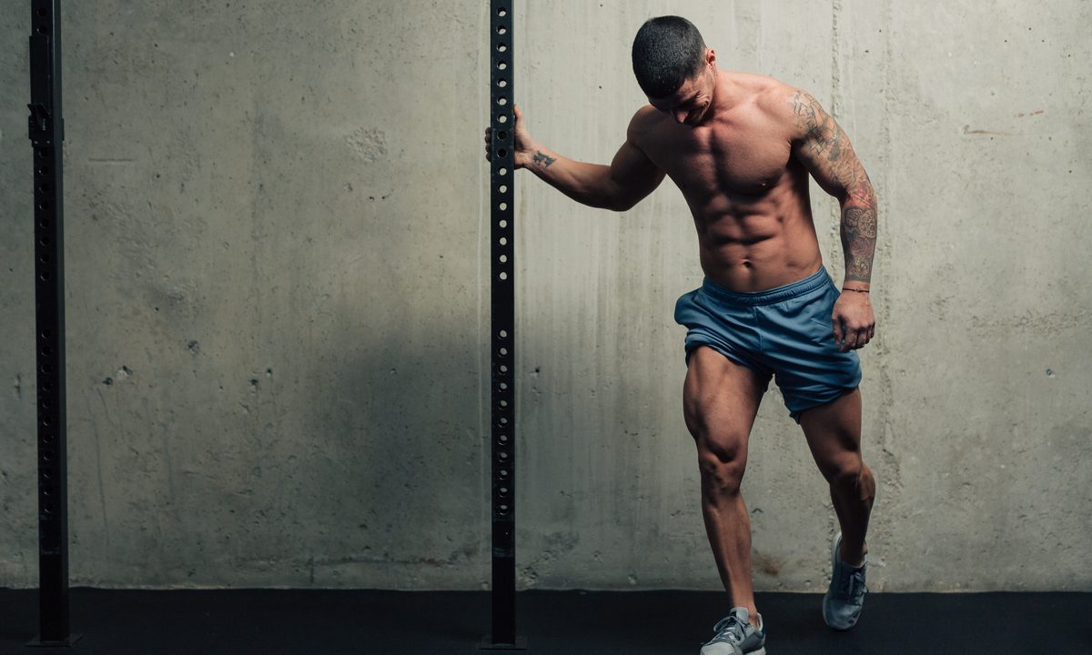 Young strong man posing and flexing his quadriceps legs muscles in a gym blue shorts holding