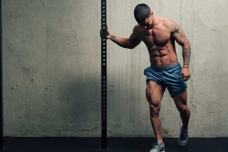 Young strong man posing and flexing his quadriceps legs muscles in a gym blue shorts holding