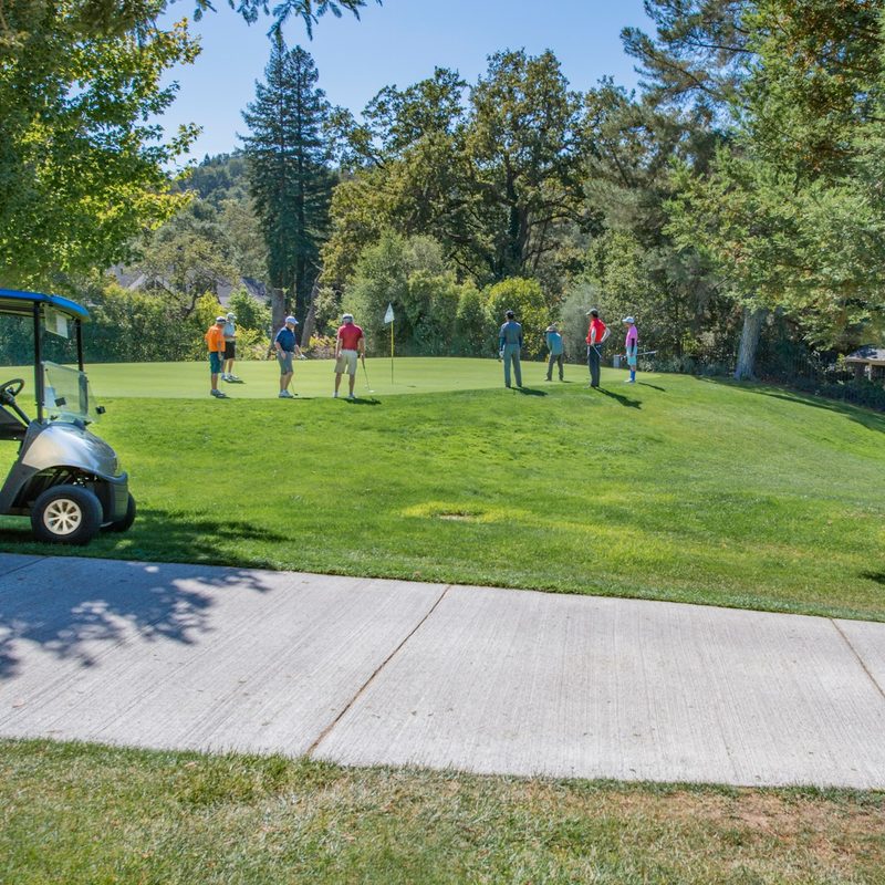 Golfers playing on a course with a golf cart to the side