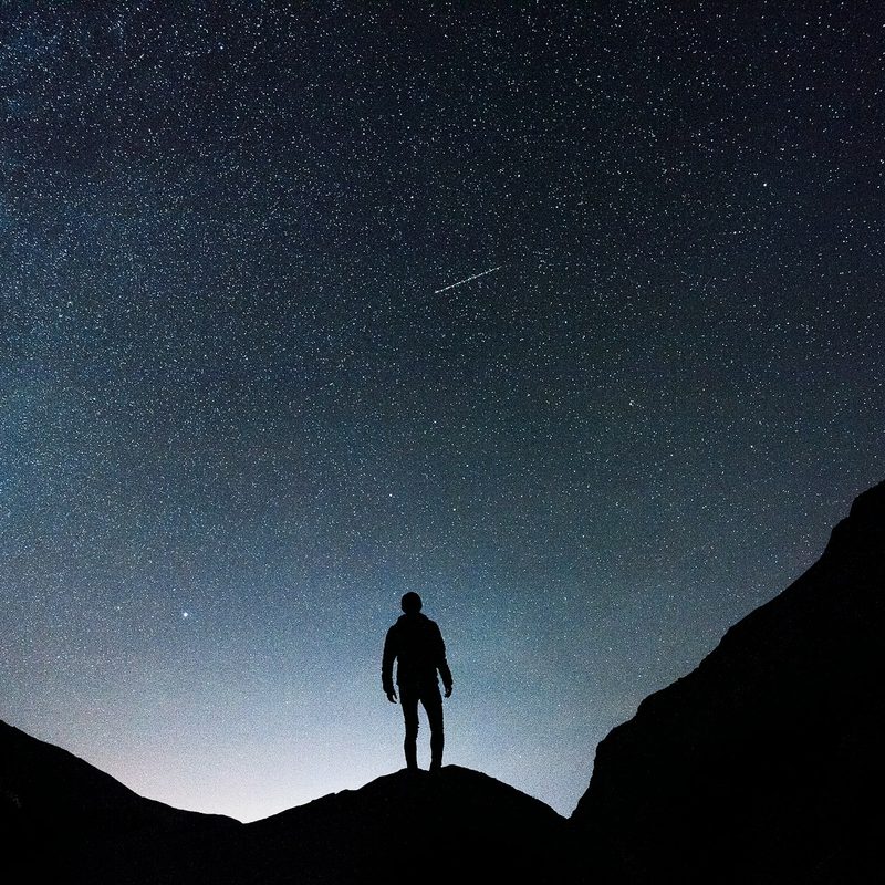A man standing on a hill while watching a shooting star