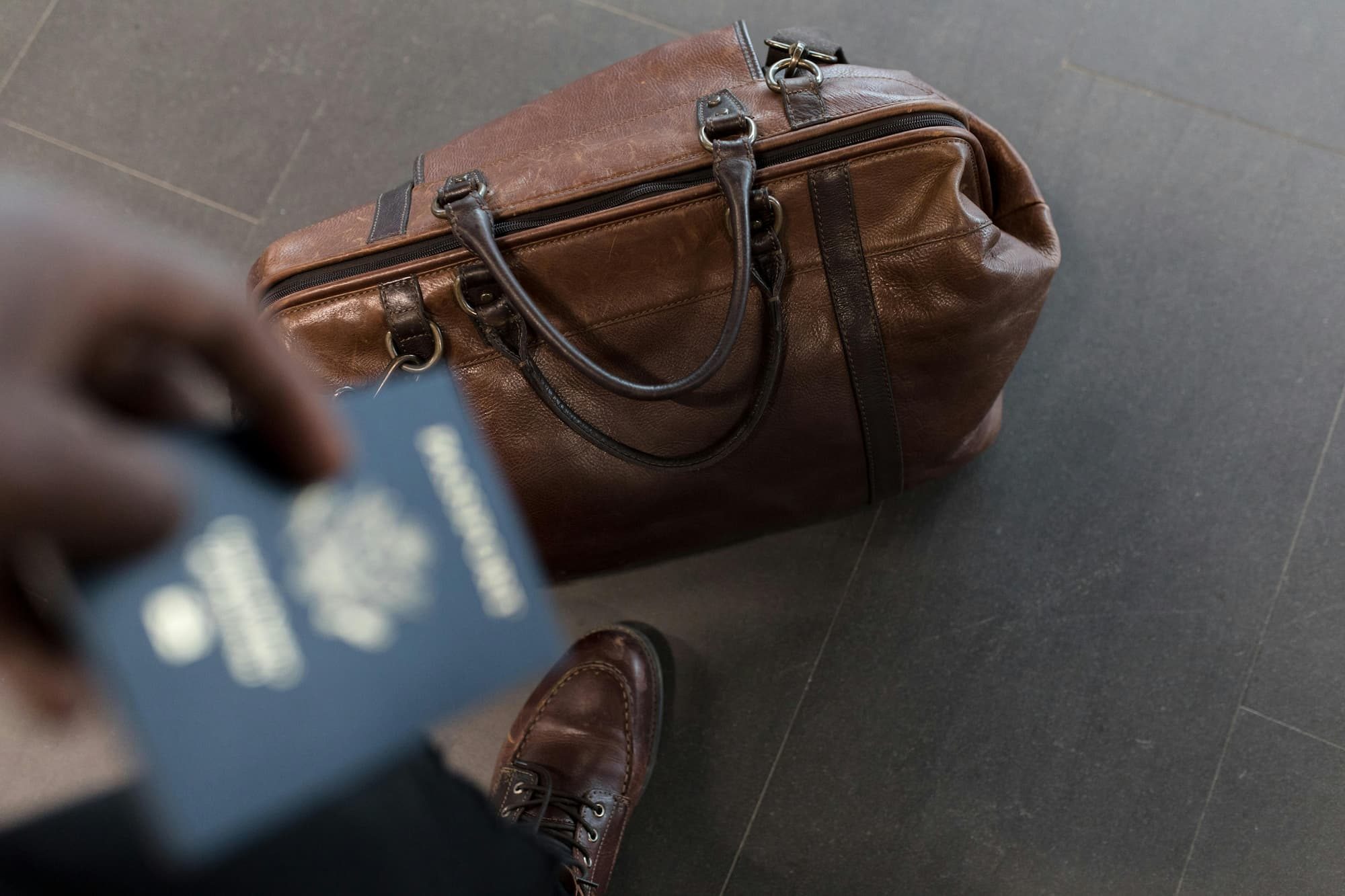 person holding passport and a duffel bag on the ground