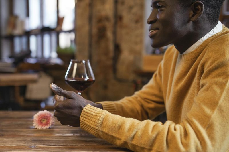 Man wearing a yellow sweater drinking wine