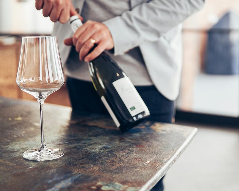 Person opening wine bottle with empty wine glass