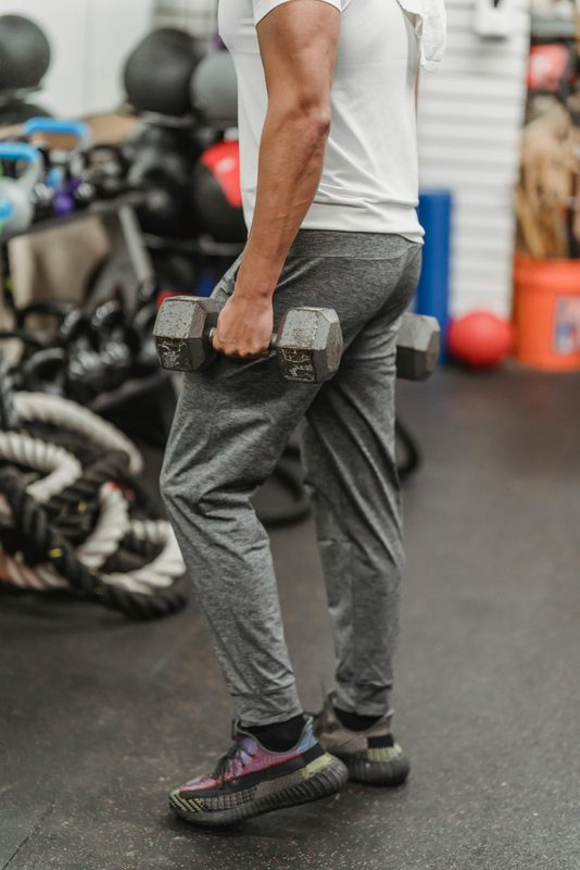 close up of man lower body gym clothes in gym holding dumbbell