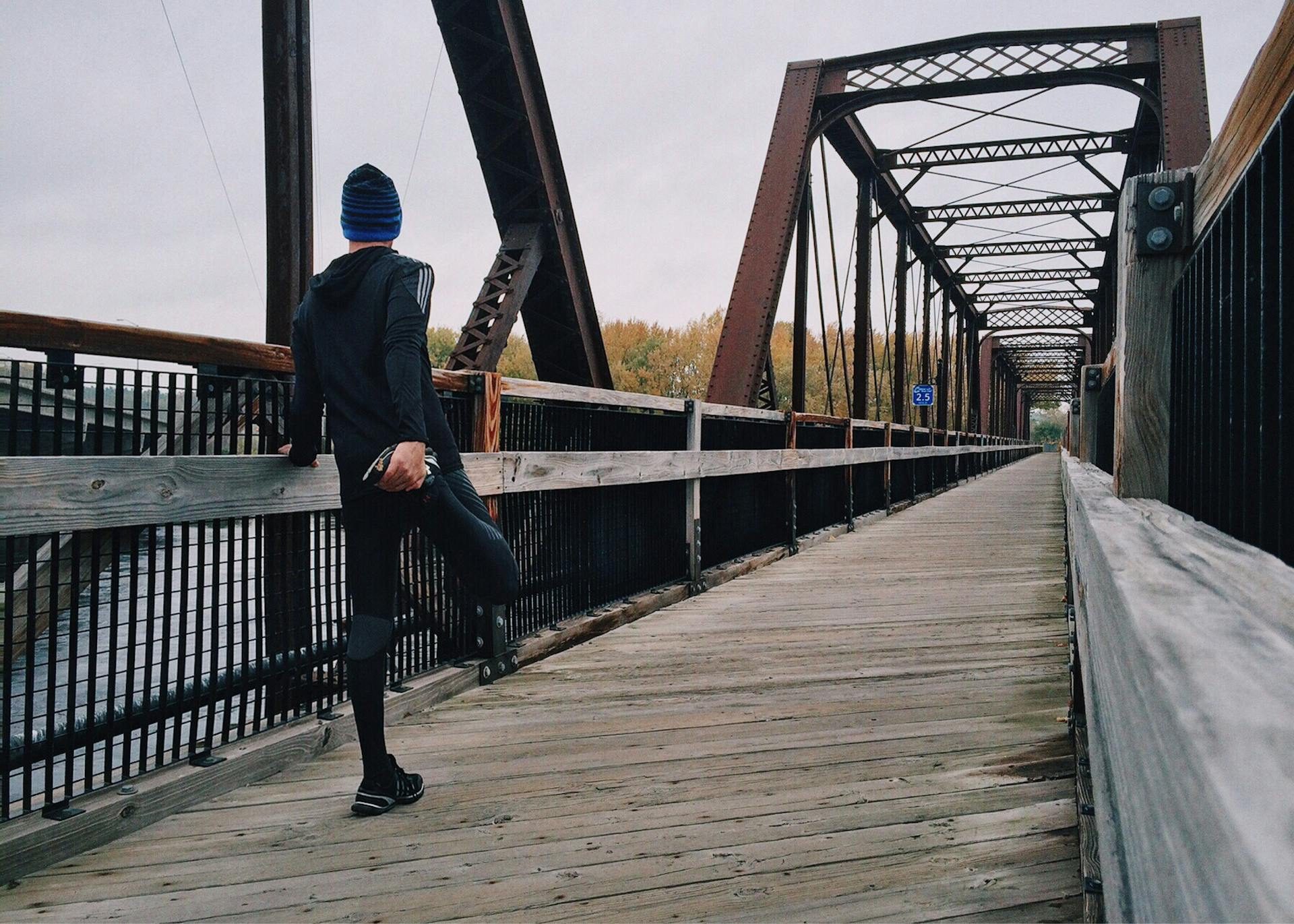 Man on bridge facing away from camera and stretching right hamstring