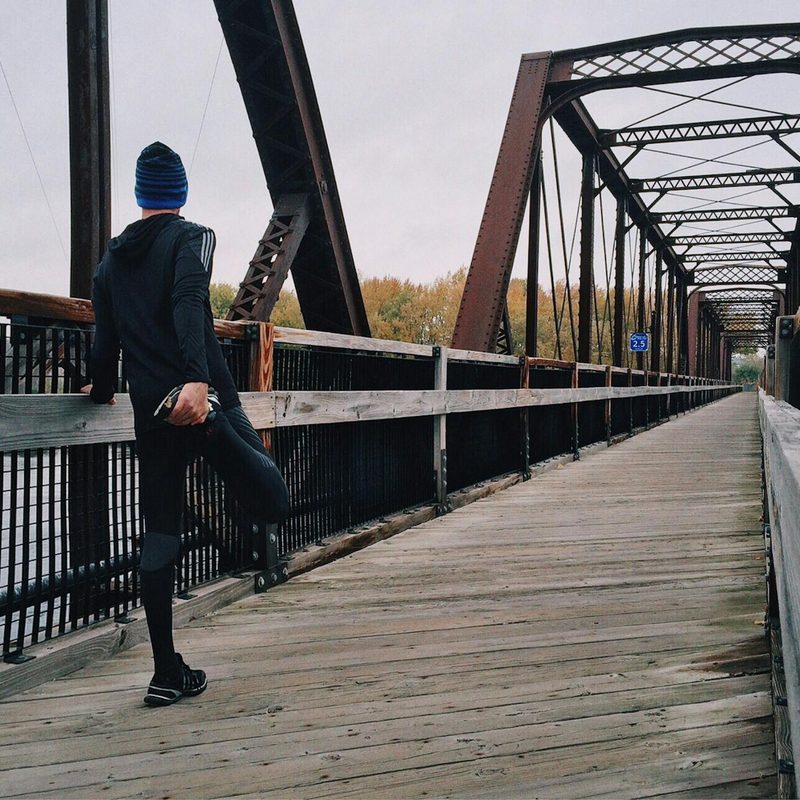 Man on bridge facing away from camera and stretching right hamstring