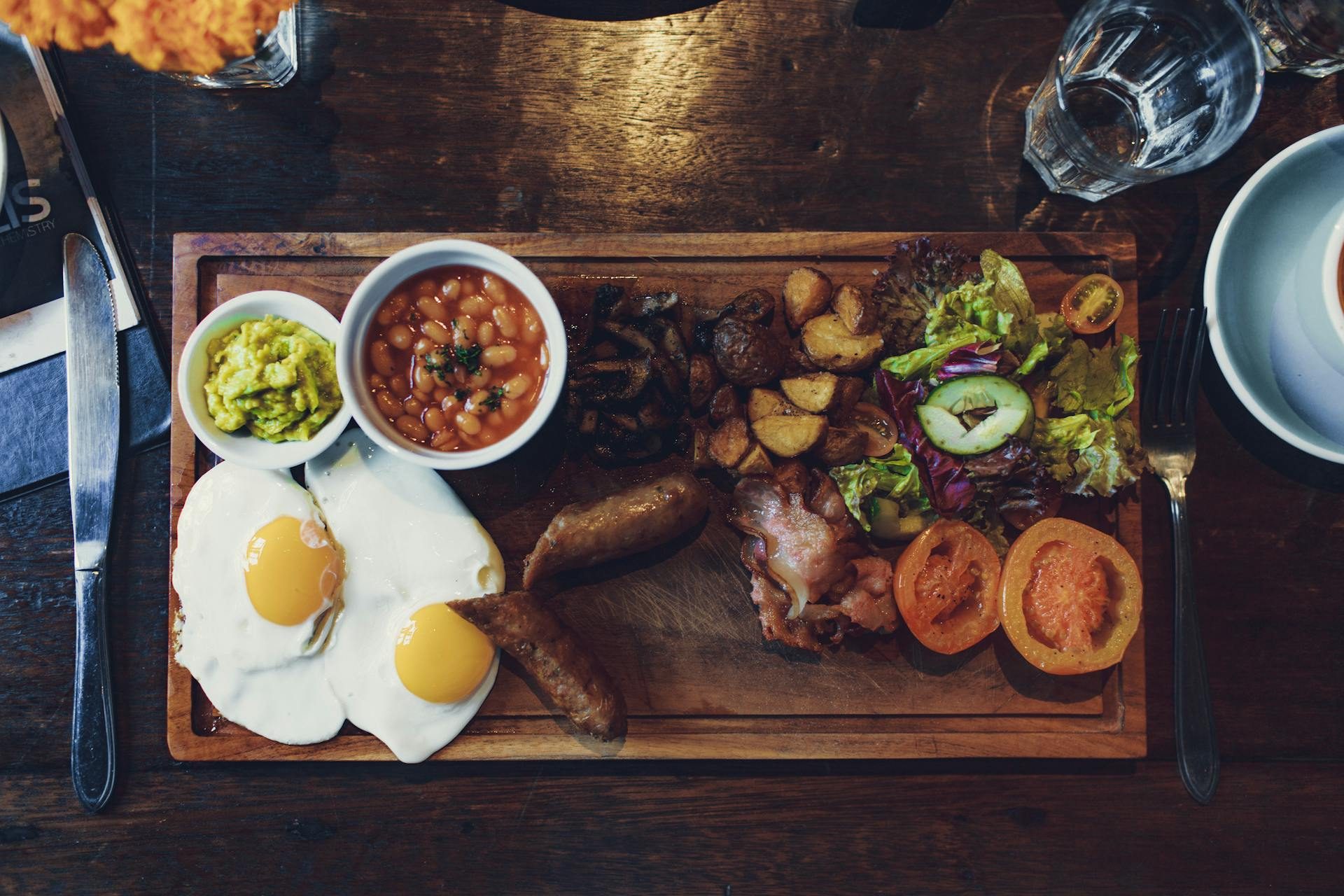Cutting board with cooked steak, fried eggs, beans, vegetables
