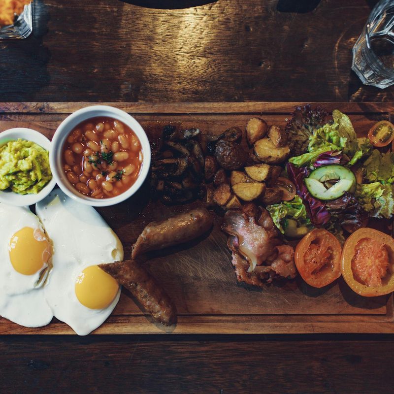 Cutting board with cooked steak, fried eggs, beans, vegetables
