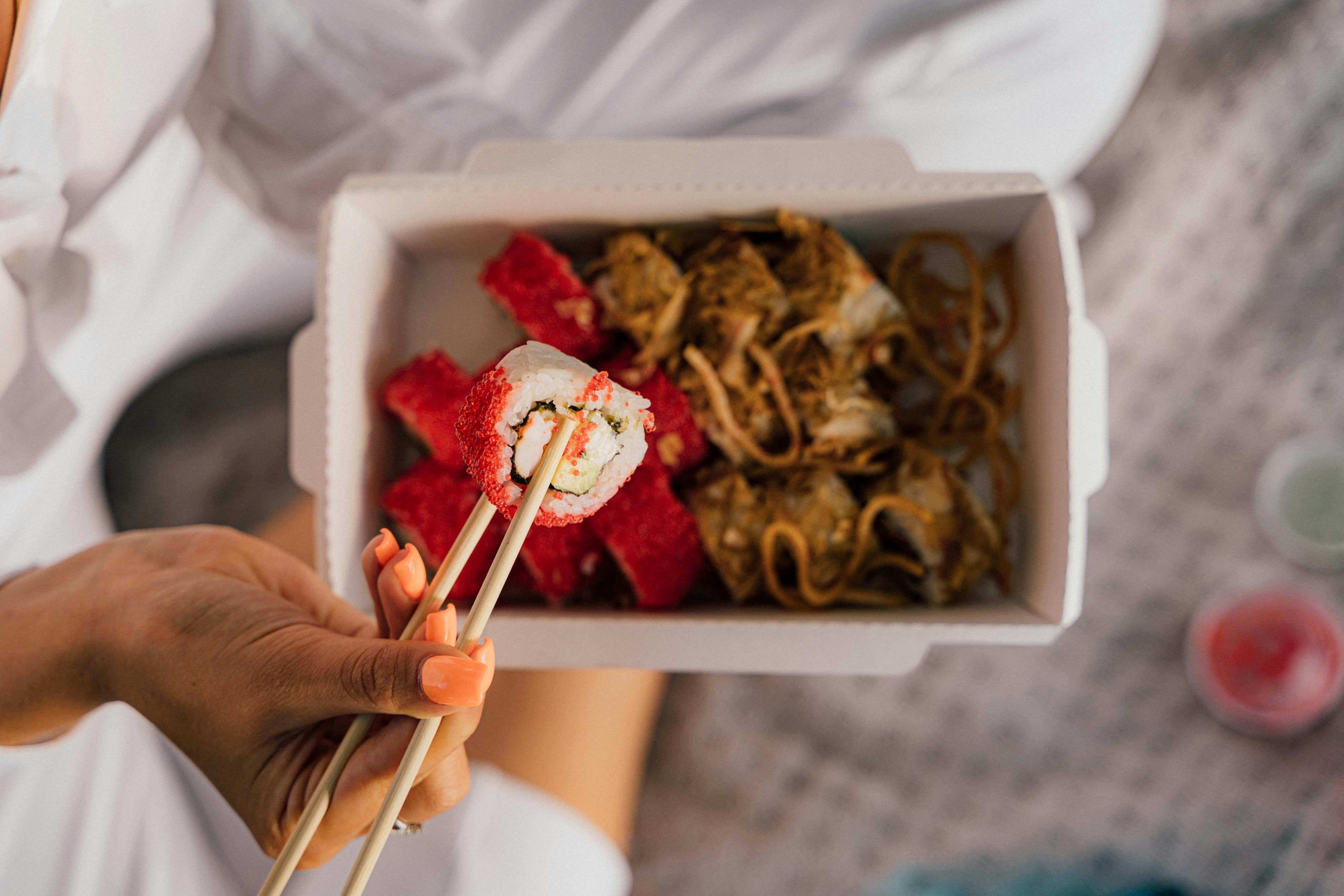 Closeup person holding sushi roll with chopsticks