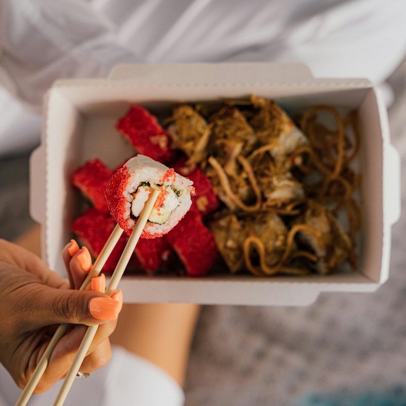 Closeup person holding sushi roll with chopsticks