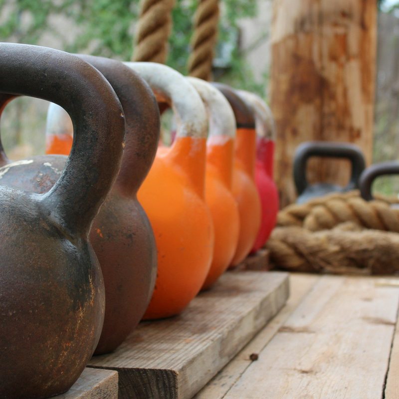 Line of kettlebells on wooden deck outside next to ropes