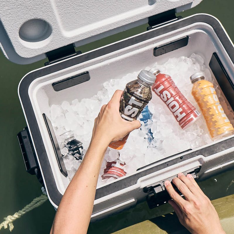 Hands grabbing a drink from an ice-filled Rugged Road floating cooler.