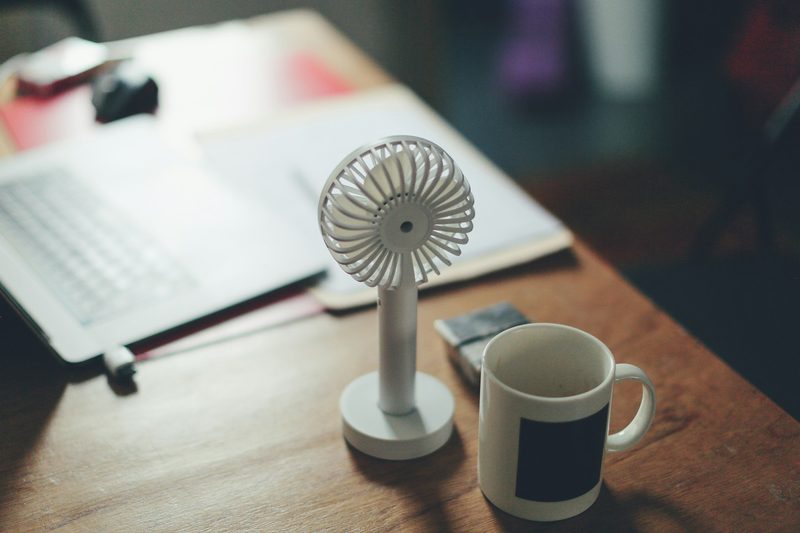 Small white portable fan on a wooden desk.