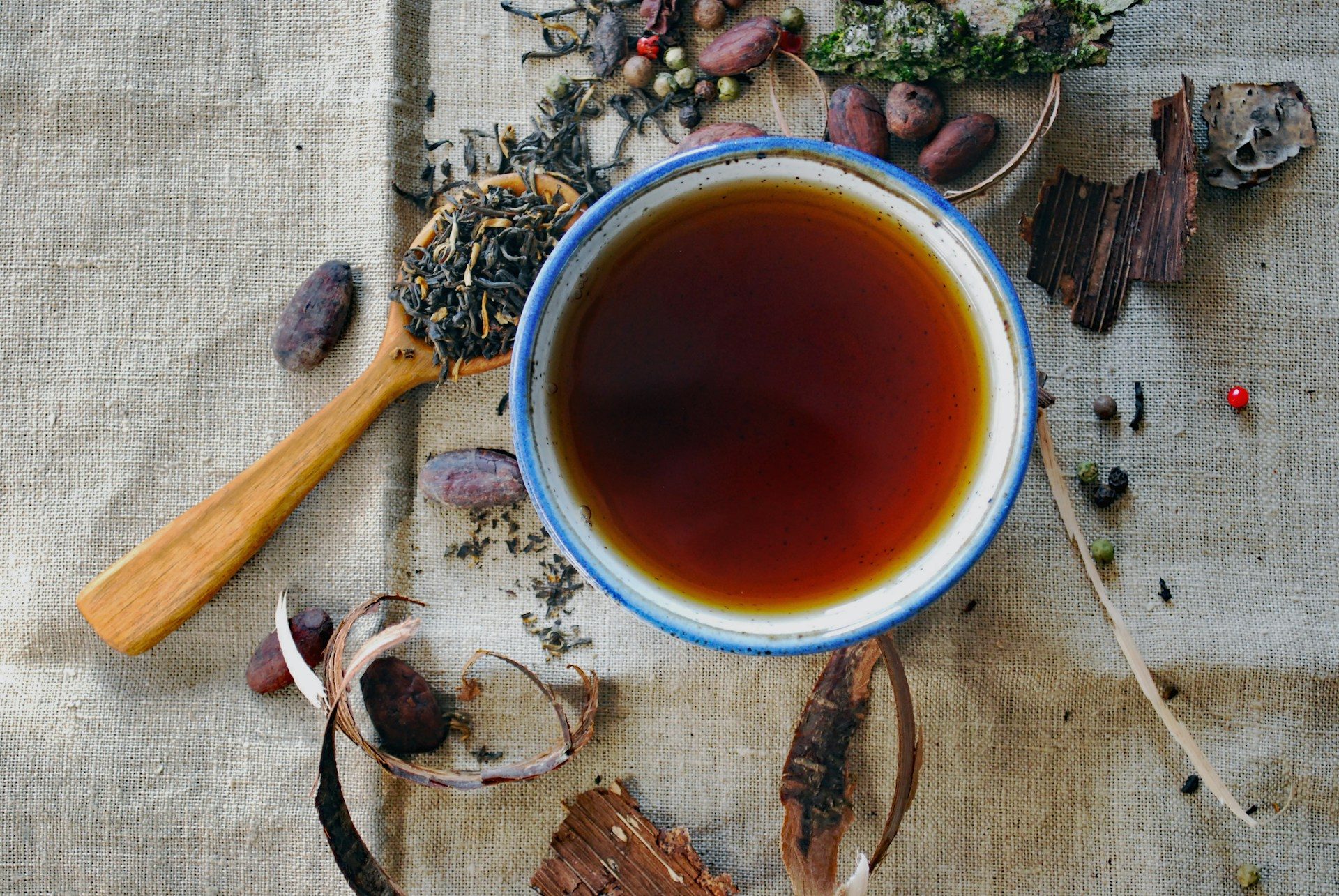 A cup of tea with tea leaves in spoons by it.