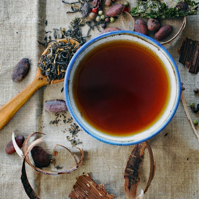 A cup of tea with tea leaves in spoons by it.