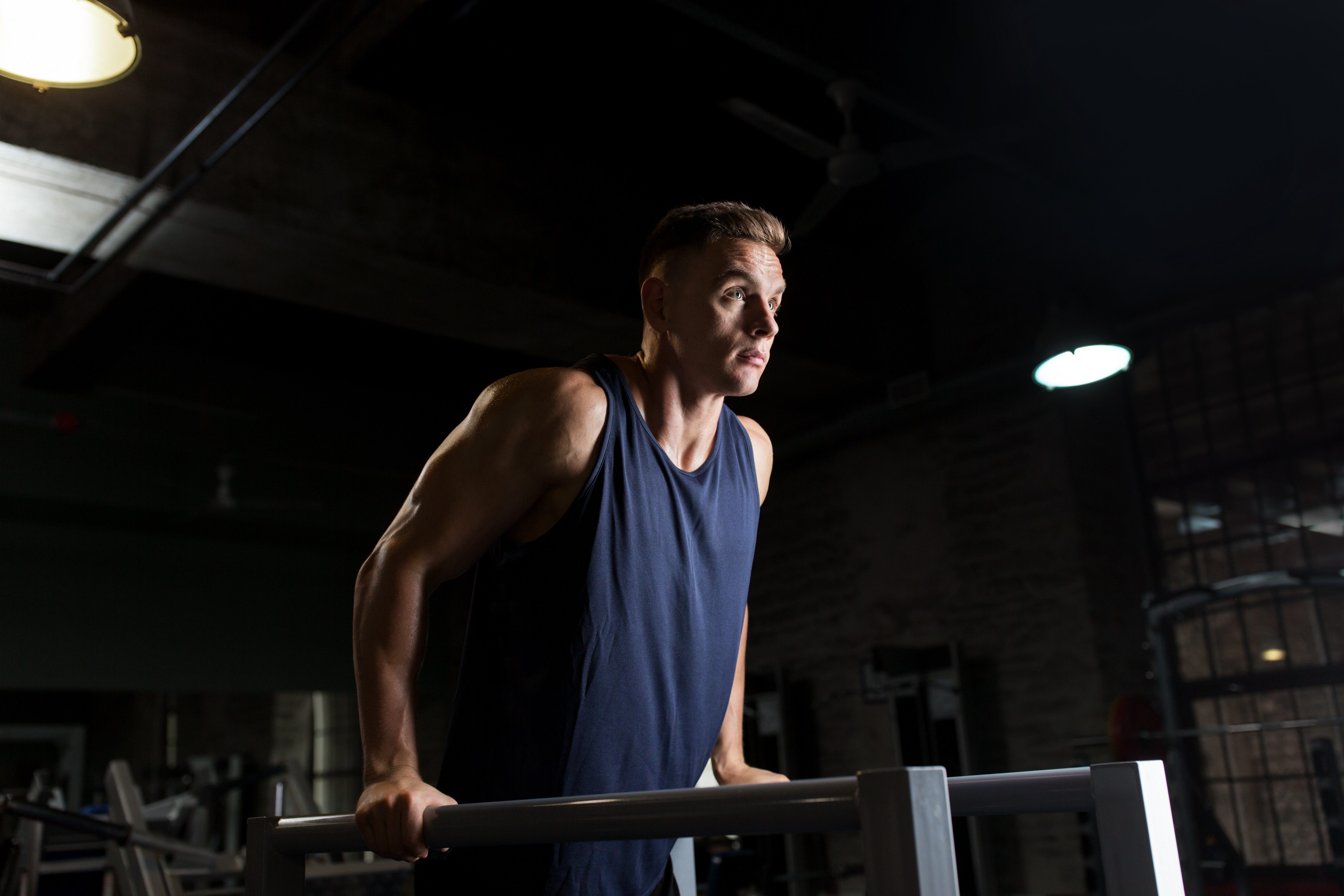 fitness, sport, bodybuilding and people concept - young man doing triceps dip exercise on parallel bars in gym