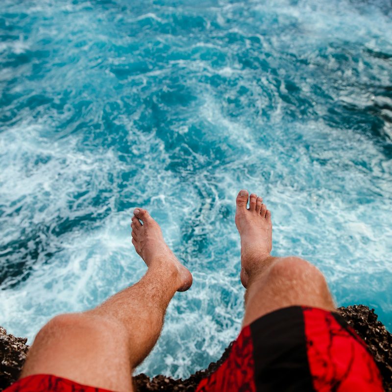 Close-up of man wearing red shirts sitting on rock looking out over blue water nature