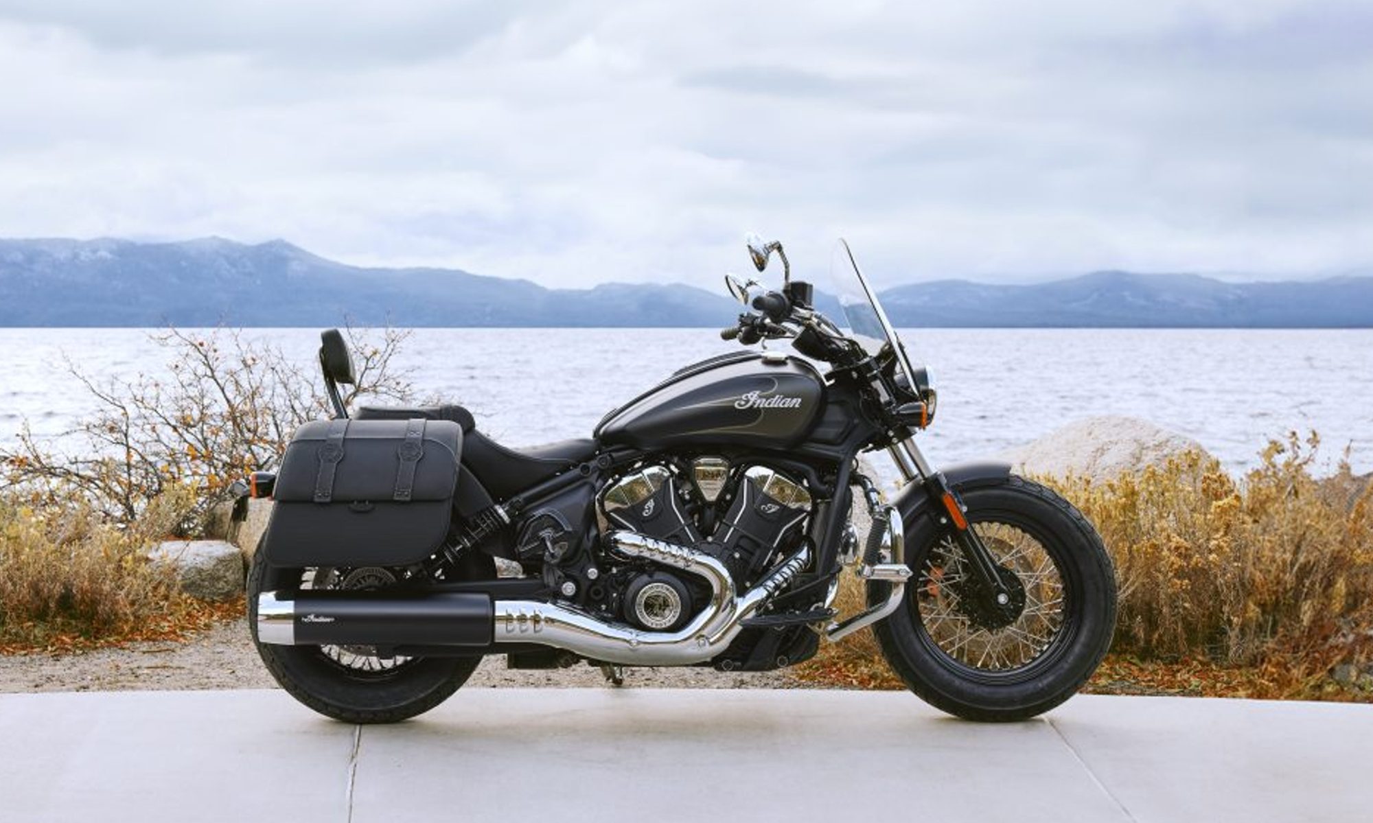2025 Indian Super Scout parked on pavement with a lake and mountains in the background right profile view.