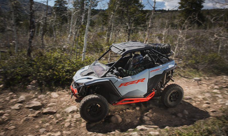 2025 Polaris ORV RZR Pro XP Sport driving along a rocky washed out creek trail in forested lands.