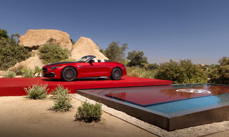2026 Mercedes-Maybach SL 680 Monogram Series red and black on a red platform next to a swimming pool and desert plants with top down.