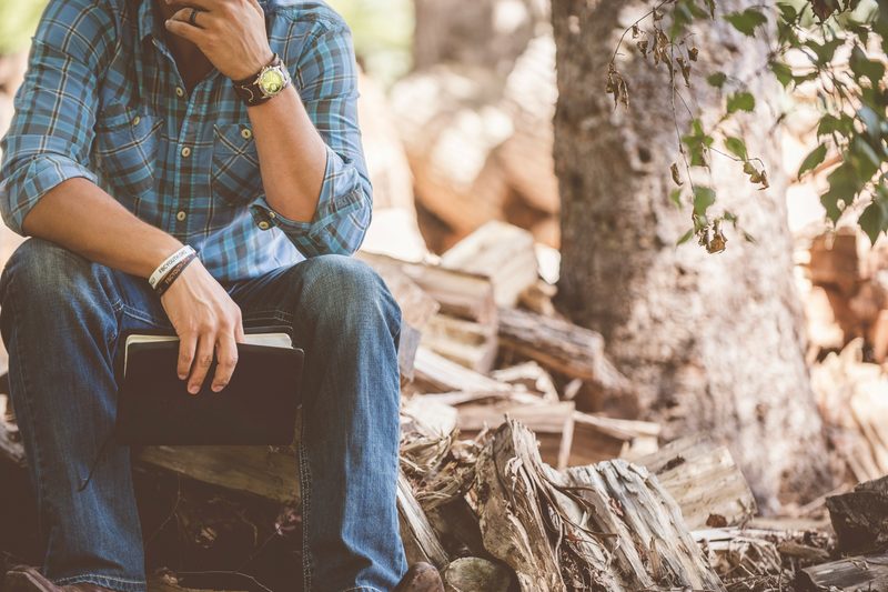 Man in flannel sitting on log with book and bracelets