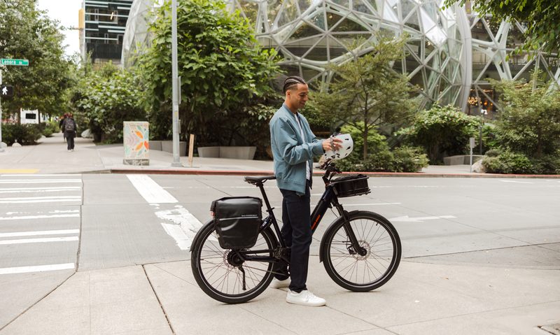 Rider putting on a helmet standing on a city sidewalk to ride a RadKick belt drive model.