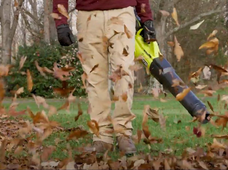 A man blows leaves away from his lawn with the Ryobi 40V HP Brushless Whisper Series cordless leaf blower.