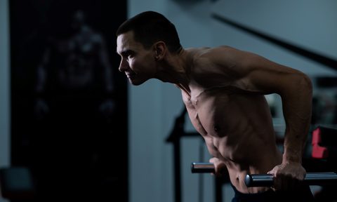 Shirtless man doing chest dips on a machine in gym