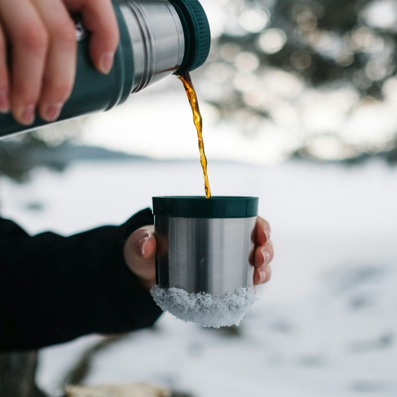 Closeup of a person pouring hot coffee from a thermos while outside in the snow.