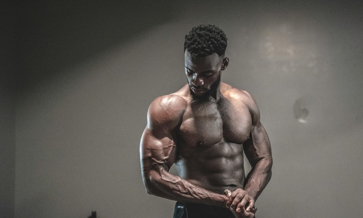 a man with a 6 pack standing against a wall with a shadow.