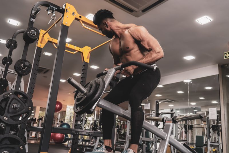 Muscular shirtless man doing T-bar row on machine in gym