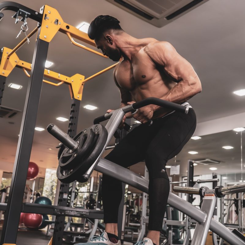 Muscular shirtless man doing T-bar row on machine in gym