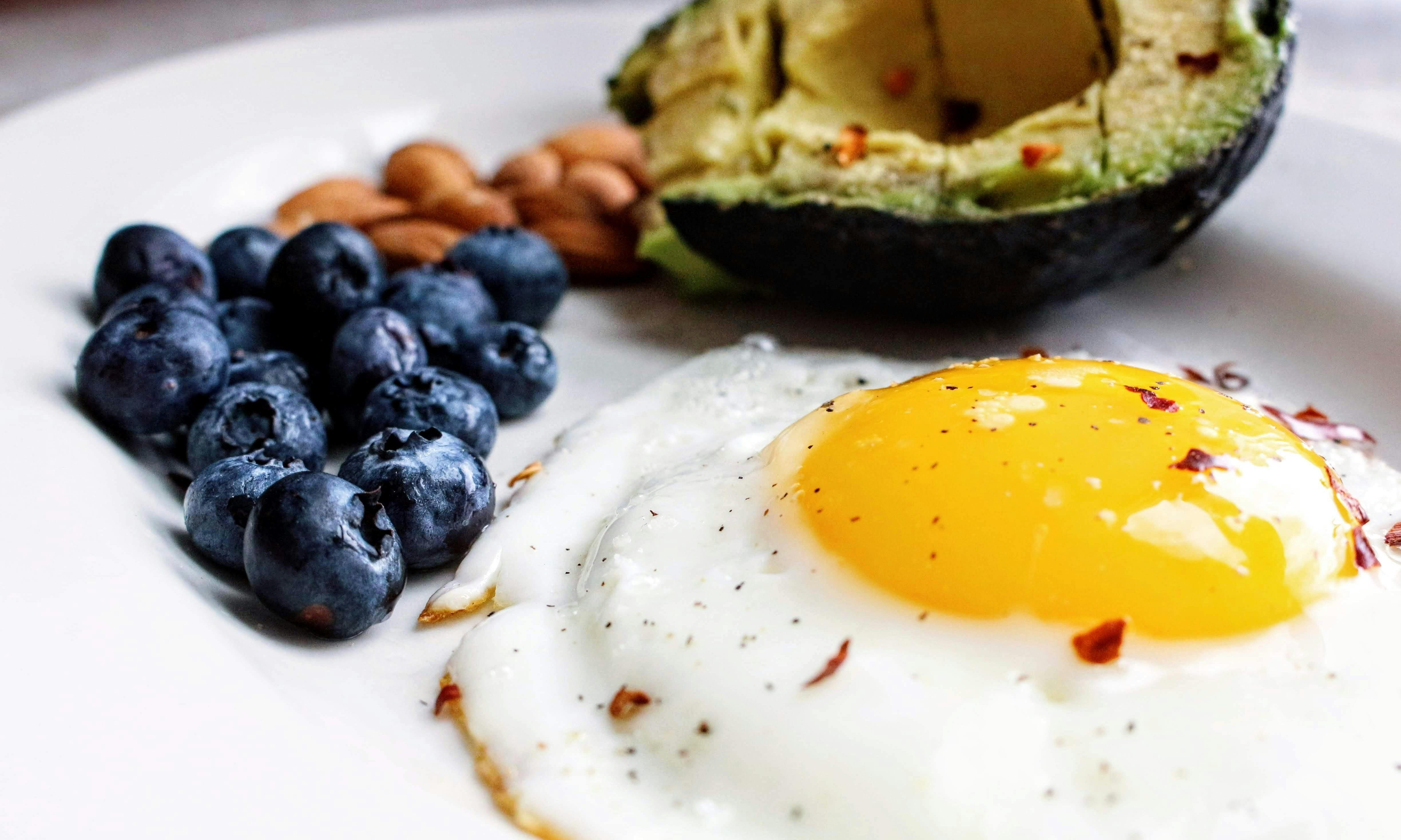 Plate with fried egg, blue berries and half an avocado.