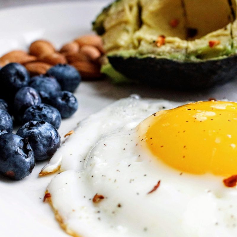 Plate with fried egg, blue berries and half an avocado.